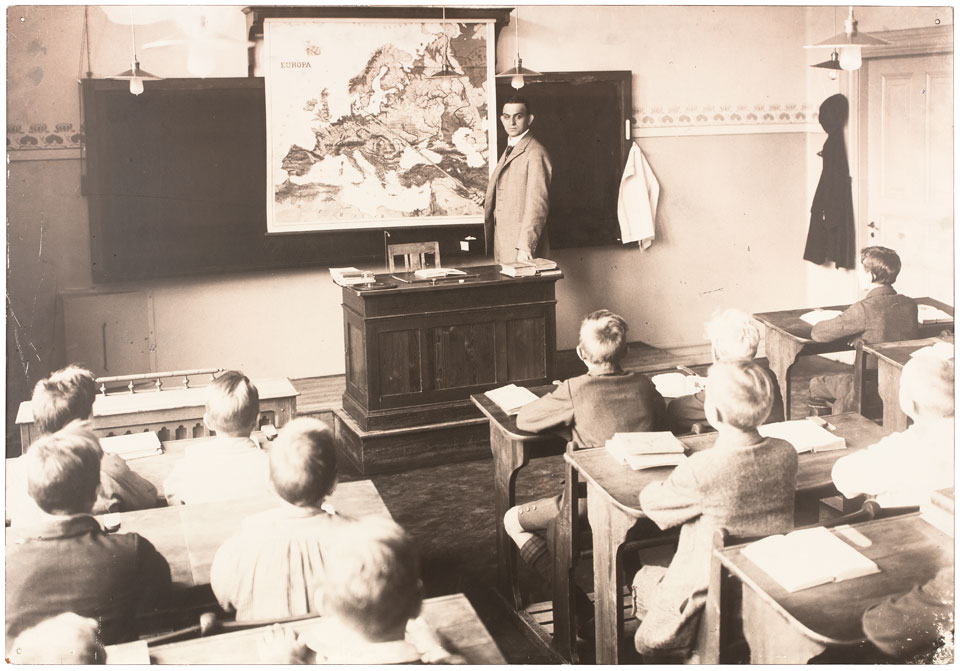 Bild på lärare och elever. Läraren pekar på en Europakarta