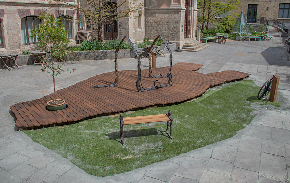 Överblick där man ser platån, bänken, trädet, hjulet och skulpturen som föreställer de lindade skorna.