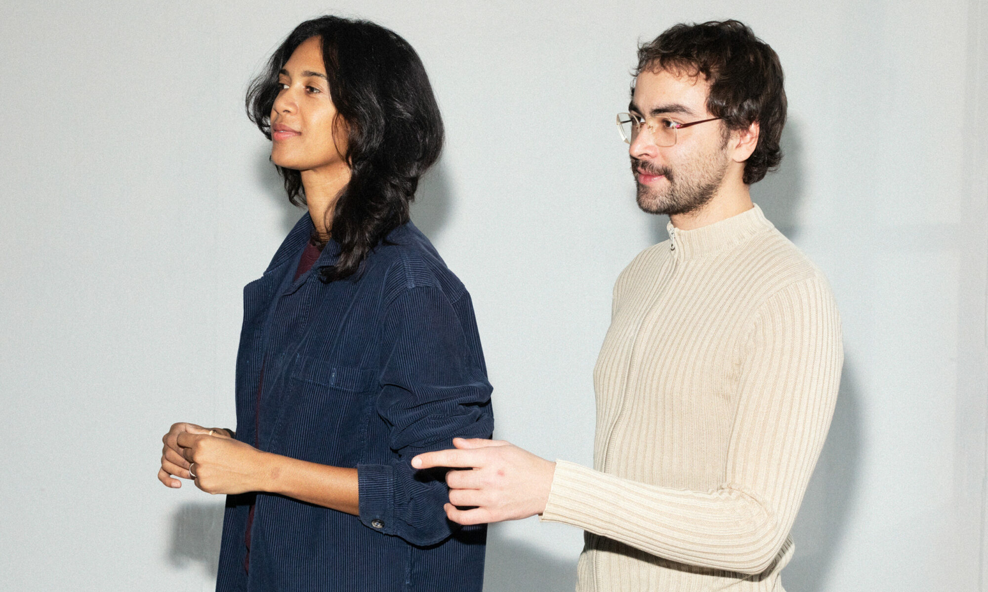 En kvinna och en man står vända mot vänster och tittar mot något utanför bilden. Mannen pekar på det vi inte ser.