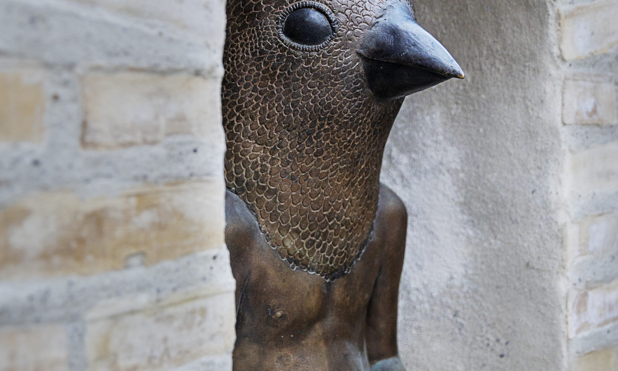 Ett foto av ett konstverk av tegel och brons som står integrerad mellan flerfamiljshus på en gågata.
